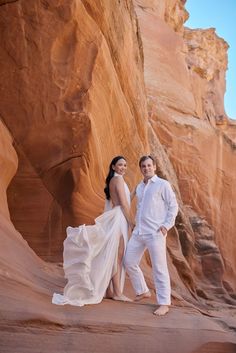 a man and woman standing in front of a rock formation at the base of a cliff