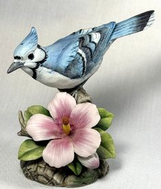 a blue bird sitting on top of a flower next to a white and pink flower