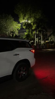 a white suv parked on the side of a road at night with its lights on