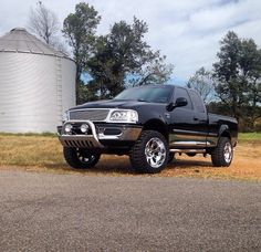 a black pickup truck parked in front of a silo on the side of a road