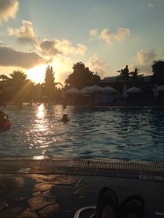 the sun is setting over an outdoor swimming pool with people in it and umbrellas