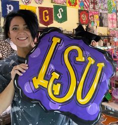 a woman holding up a purple and yellow sign with the word lsu painted on it