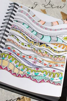 an open notebook with colorful designs on the pages and writing underneath it, sitting on a table