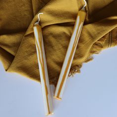 two yellow and white candles sitting on top of a cloth