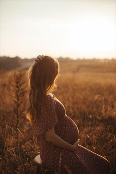 a pregnant woman sitting on top of a wooden bench in a wheat field at sunset