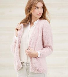 a woman is wearing a pink cardigan sweater and white shirt while standing in front of a wall