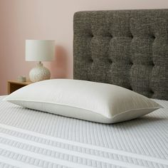 a white pillow sitting on top of a bed next to a nightstand with a lamp