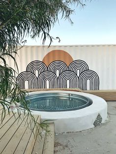 an outdoor hot tub in front of a wall with art work on the back side