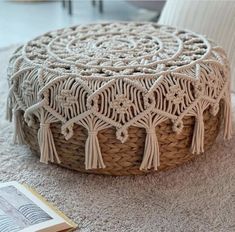 a woven basket with tassels on the floor next to a book and chair