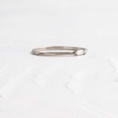 a white gold ring with a single diamond in the middle on a plain surface,