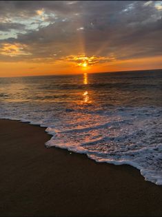 the sun is setting over the ocean with waves crashing in front of it and some clouds