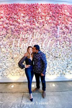 a man and woman standing in front of a flower wall with the words happy valentine written on it