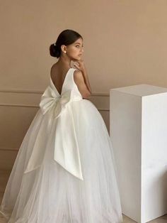 a woman standing next to a white box wearing a dress with a bow on it