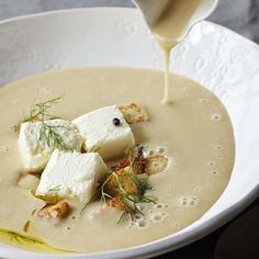 a white bowl filled with soup and topped with croutons, cheese and herbs