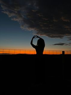 the silhouette of a woman making a heart shape with her hands in front of a fence