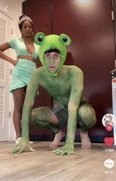 two women standing in front of a green frog costume