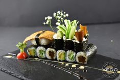 sushi rolls are arranged on a black plate with garnishes and vegetables