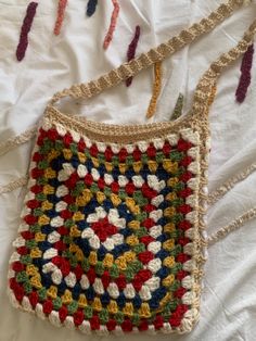 a crocheted purse sitting on top of a white bed covered in multicolored yarn