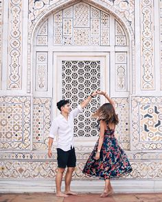 an engaged couple dancing in front of a white wall with intricate carvings on it's walls