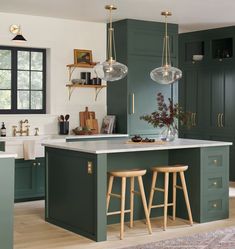 a kitchen with green cabinets and stools in the center, an island counter is flanked by two pendant lights