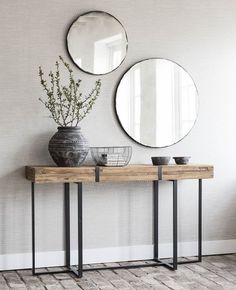 two round mirrors on the wall above a wooden table with metal legs and a potted plant