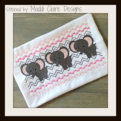 an elephant cross stitched on top of a white piece of cloth with pink and black trim