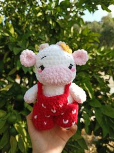 a hand holding a small crocheted pig in a red and white dress with hearts on it