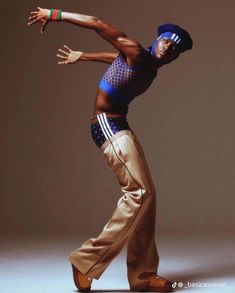 a man is dancing with his arms extended in the air while wearing brown pants and a blue tank top