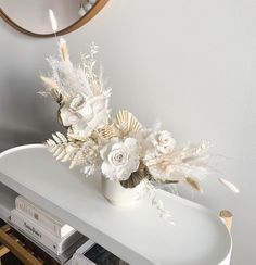 a white vase with flowers and feathers on a table in front of a round mirror