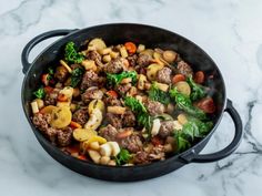 a skillet filled with meat, vegetables and potatoes