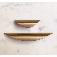 two brass handles on a white marble countertop, one is shaped like an oval and the other is curved