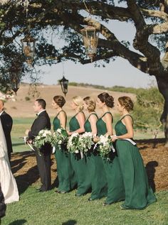 a group of people standing around each other in front of a tree and grass field