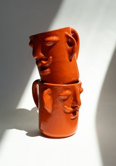 two orange mugs with faces on them sitting side by side against a white wall