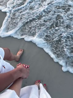 two people are sitting on the beach with their feet in the sand near the water