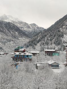 snow covered mountains and houses in the foreground, with trees on either side of them