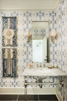 a bathroom with blue and white wallpaper has a sink, mirror and two lights