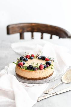 a cheesecake with berries on top sits on a table next to a fork and spoon