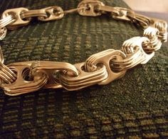 a close up of a gold chain bracelet on a green cushion with the clasp undone