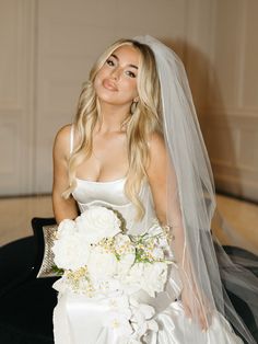 a woman in a wedding dress sitting on a chair with her veil over her head