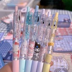 a person holding four different colored pens in their hand with hello kitty stickers on them