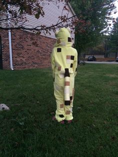 a person in a yellow costume standing on the grass near a tree and building with cars parked behind it