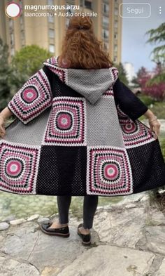 a woman in a black and white crocheted coat is standing on a rock