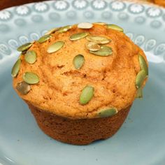 a muffin with pumpkin seeds on top sits on a blue plate next to some bread