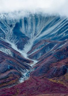 the mountains are covered in snow and brown grass, with low lying clouds above them