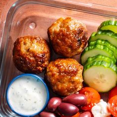 a plastic container filled with meatballs, vegetables and ranch dressing next to cucumbers