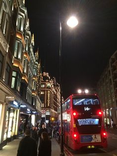 a red double decker bus parked on the side of a street next to tall buildings