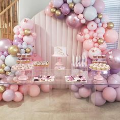 a table topped with lots of pink and gold balloons next to a wall filled with desserts