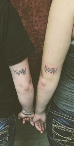 two people holding hands with tattoos on their arms