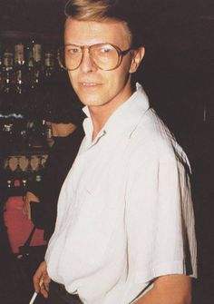 a man with glasses standing in front of a bar holding a knife and looking at the camera