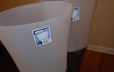 two white plastic containers sitting on top of a wooden table next to a wall and wood floor